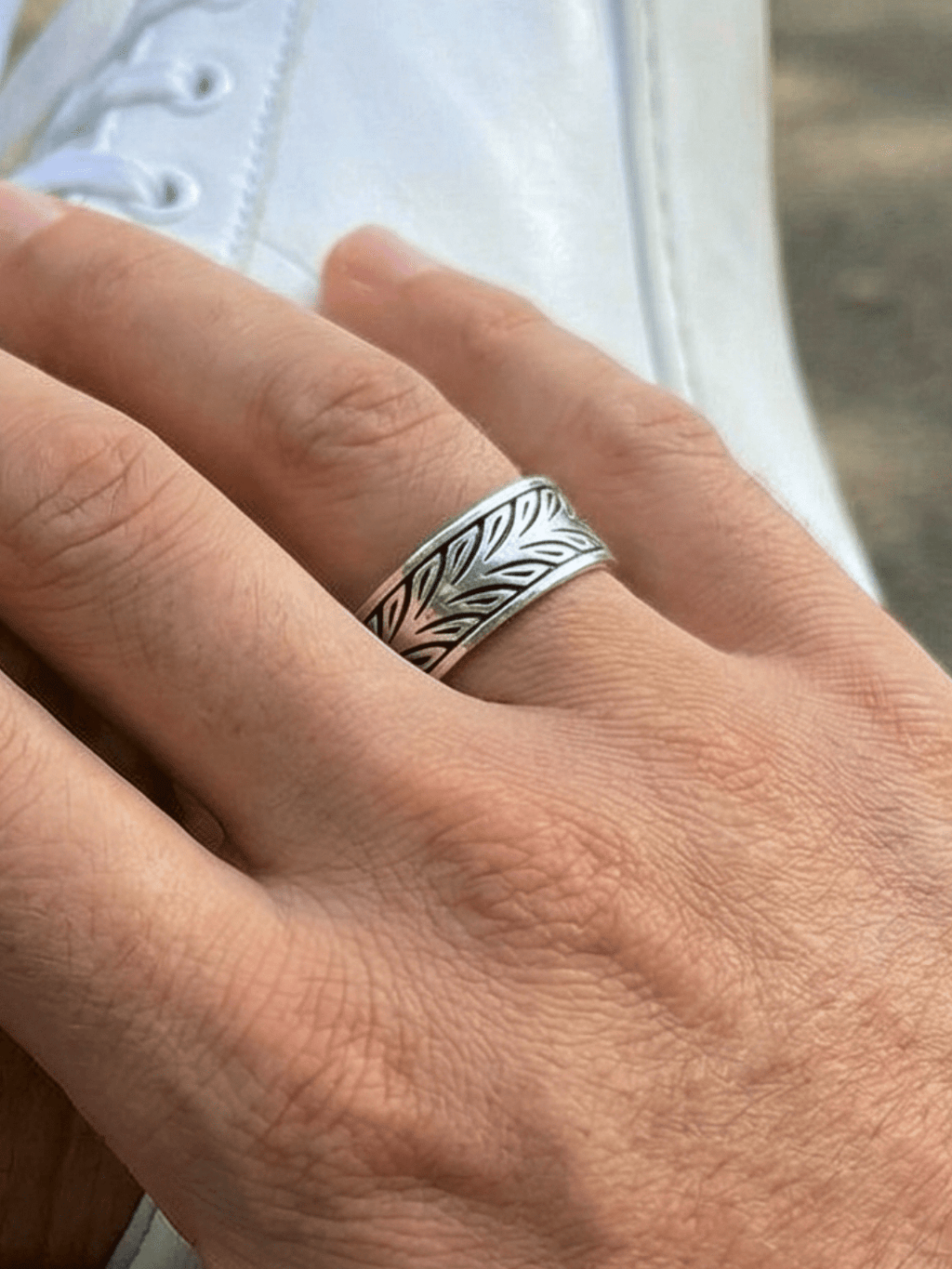 Foto vom Twin Leafs Ring an einer Hand, die einen Knöchel umgreift, im Hintergrund ein weißer Schuh und unscharf zu erkennen ein Stadtpark